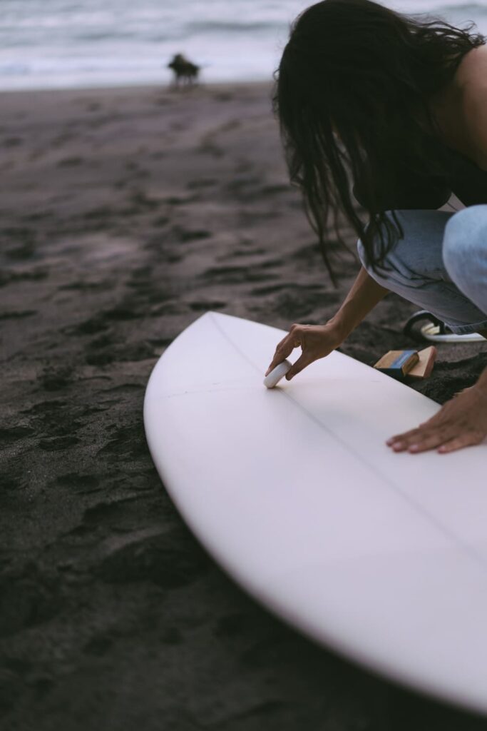 young woman surfer preparing surfboard ocean waxing woman with surfboard ocean active lifestyle water sports (1) (1)